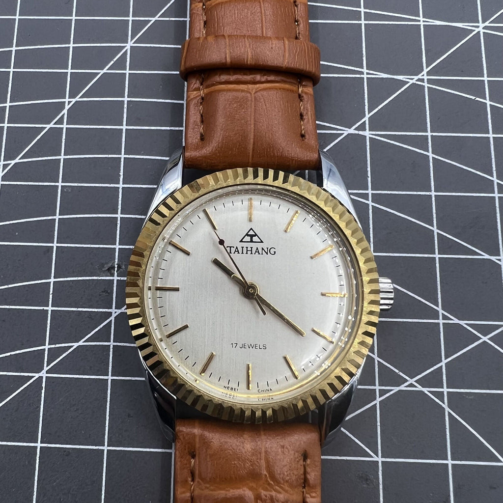 TAIHANG 38mm manual mechanical watch with golden markers, silver dial, round case, and 17 jewels for precise timekeeping.