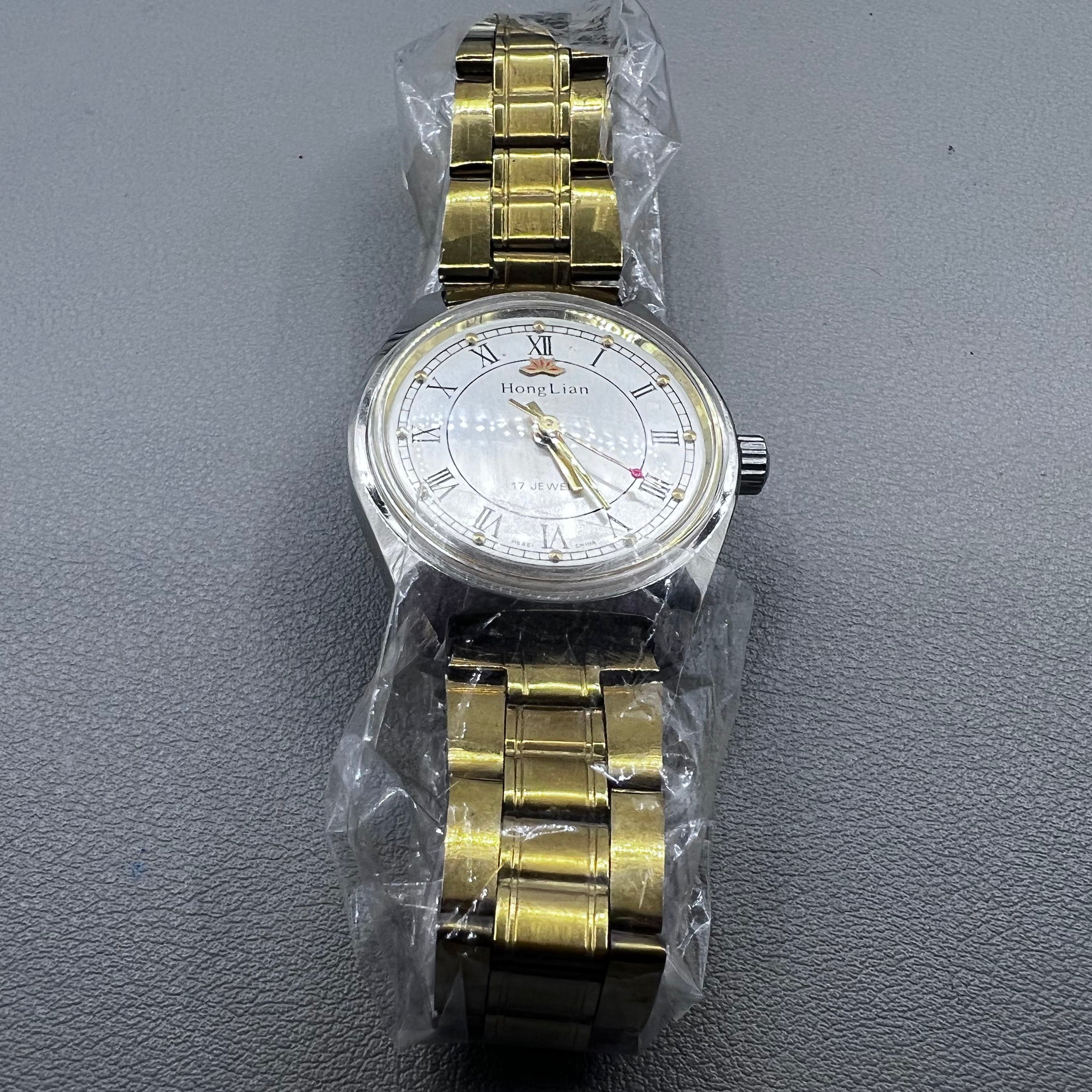 32mm golden stainless steel manual watch with 17 jewels and Roman numeral dial.